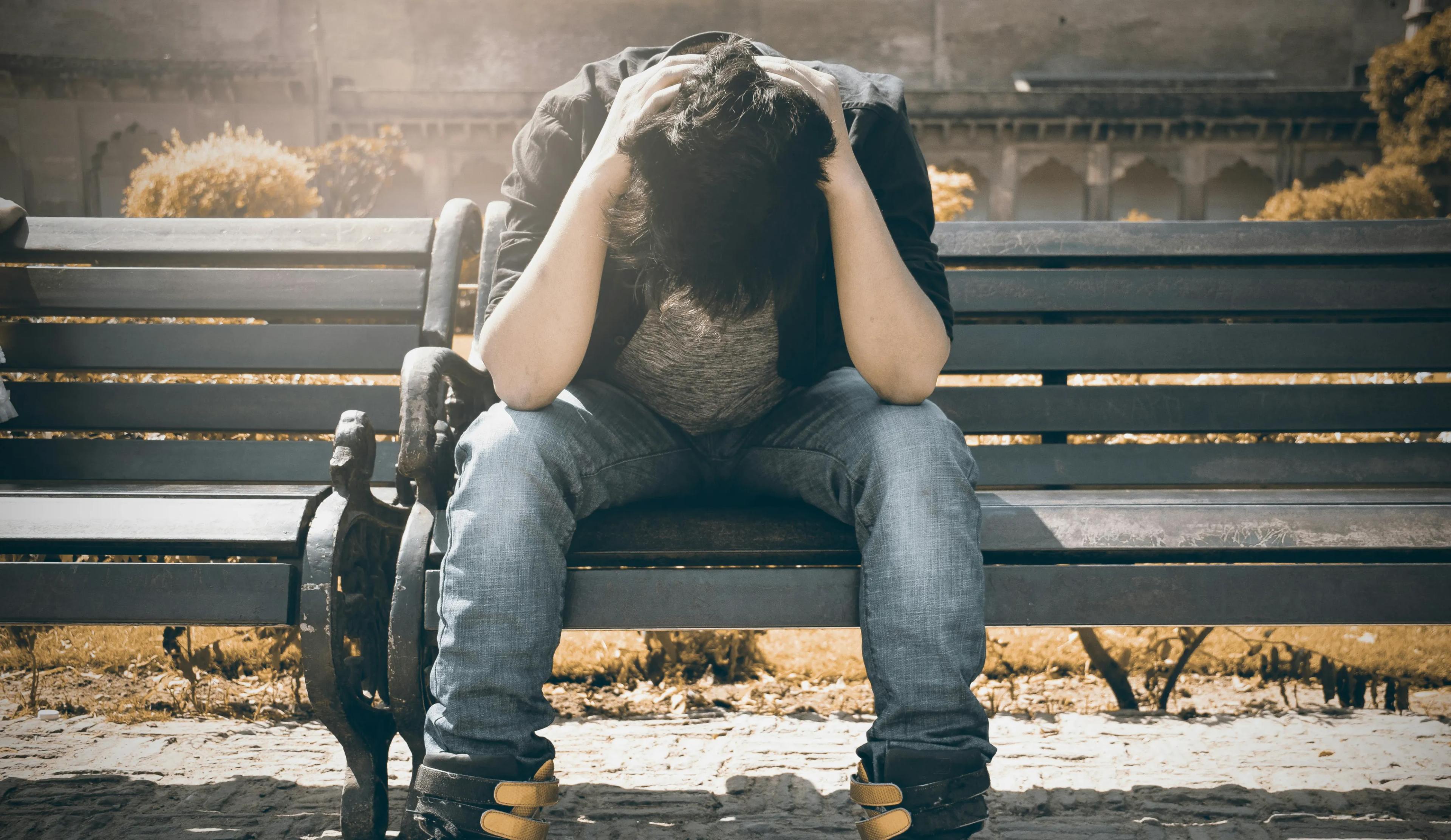 Man sitting on a bench hangs his head