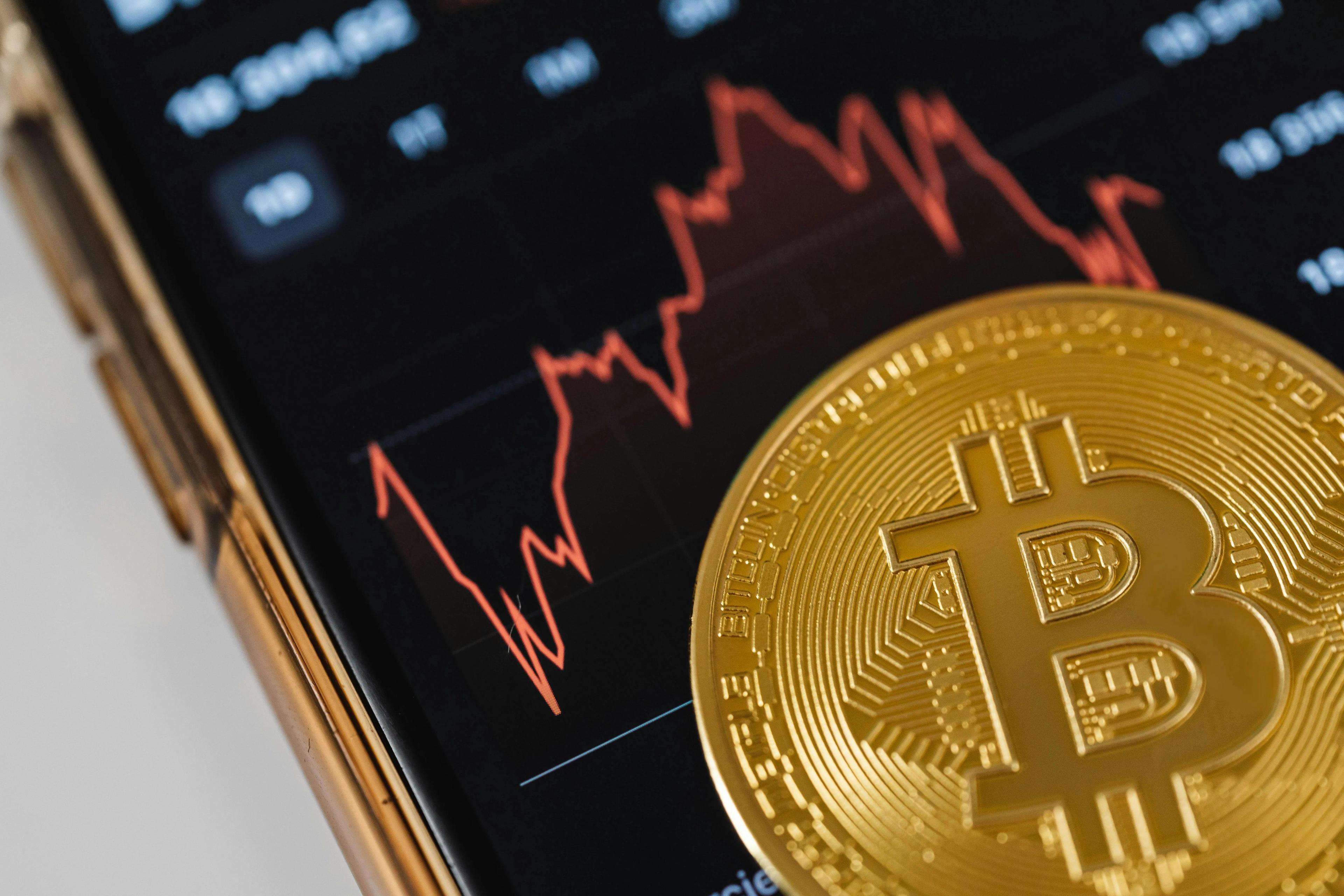 A closeup of a Bitcoin sitting on a smartphone showing a graph